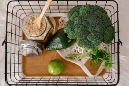A flat lay of fresh, healthy ingredients including broccoli, avocado, lime, and oats in a basket.